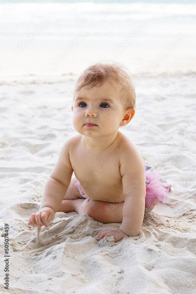 Candid portrait of adorable little baby girl on sand at beach on background of sea. Sensory development for kids outdoors. Candid portrait of adorable little baby girl on sand at beach on background of sea. Sensory development for kids outdoors.