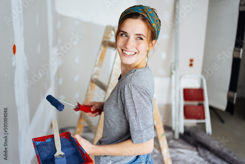 Young happy woman paints her apartment and looks back photo