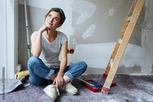 Young woman sitting in her unrenovated apartment thinking how to paint the walls photo