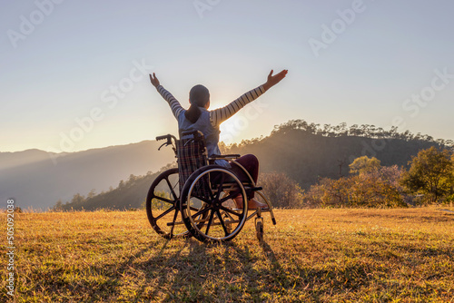 Woman sitting on a wheelchair enjoying sundown on mountain background.