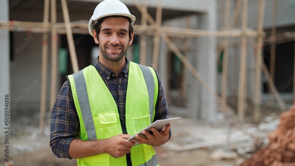 Smart male engineer specialist with safety uniform holding tablet to work making a check and inspect on construction building looking at camera with smile, Engineering working with happiness concept - obrazy, fototapety, plakaty 