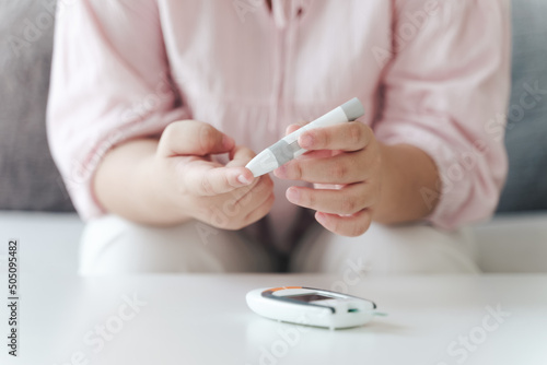 Принти на полотні Asian woman using lancet on finger for checking blood sugar level by Glucose met