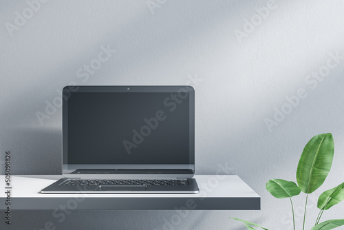 Close up of empty laptop on designer office desktop. Decorative plant and concrete wall background. Mock up, advertisement, technology, product review and webinar concept. 3D Rendering.