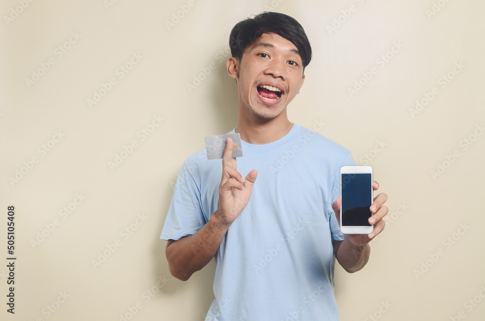 Portrait of asian young man holding smart phone and ATM card, isolated background Portrait of asian young man holding smart phone and ATM card, isolated background
