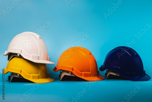 White, yellow,orange,and blue hard safety helmet hat for safety project of workman as engineer or worker, on blue background.