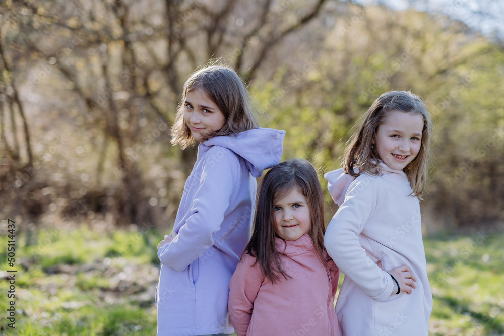 Three little sisters looking at camera in spring nature together.