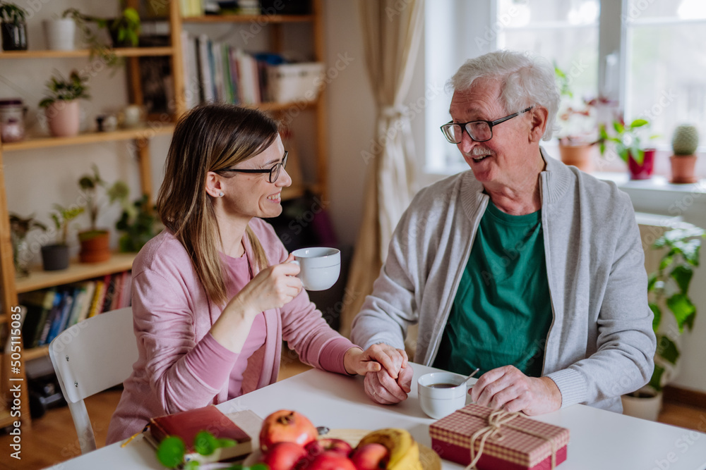 Adult daughter visiting her senior father at home and having coffee together, touching hand. Adult daughter visiting her senior father at home and having coffee together, touching hand.