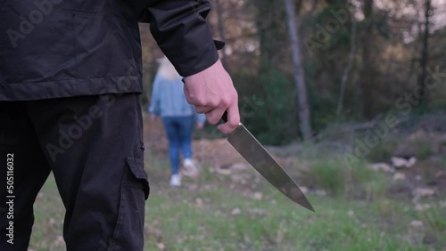 A man with a knife in the forest. The maniac pursues the victim and prepares to attack. The girl runs away from the killer photo