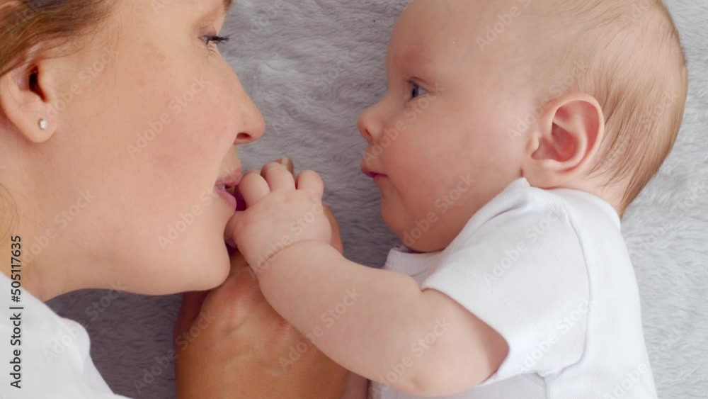 Happy newborn baby with his mother. Healthy newborn baby in a white t-shirt with mom. Closeup Faces of the mother and infant baby. Cute Infant boy and parent, top view. Slow motion. Happy family Happy newborn baby with his mother. Healthy newborn baby in a white t-shirt with mom. Closeup Faces of the mother and infant baby. Cute Infant boy and parent, top view. Slow motion. Happy family