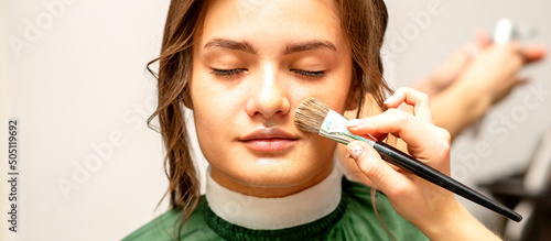 The makeup artist applies a cosmetic tonal foundation on the face using a makeup brush