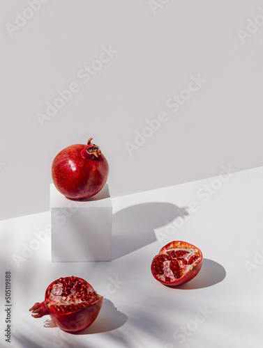 Creative composition madeof red pomegranates on sunlit backgound with white cube podium and shadows. Summer refreshment concept. Minimal style. photo