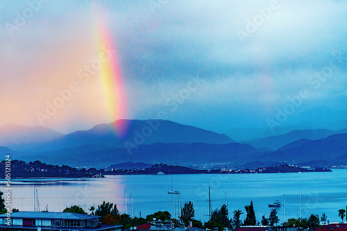 Seaside town with morning rainbow. Port town in rainy weather. An amazing atmospheric phenomeno. Beautiful rainbow over the sea