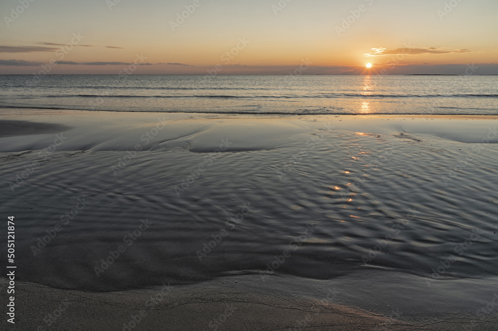Tramonto sul mare, con riflesso del sole sull'acqua e sulla spiaggia.