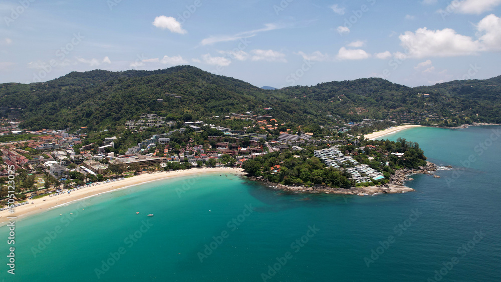 Clear water with a rocky Kata beach. The bottom is visible. Aerial view of the ocean and shore from the drone. The whole island is green. There are beautiful hotels. A tourist place in Thailand