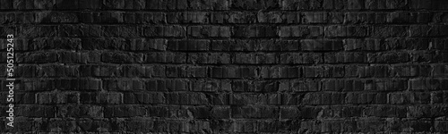 Old rough black brick wall wide texture. Gloomy grunge dark textured panoramic background