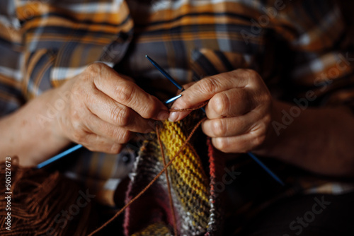 Unrecognizable woman hands of elderly woman, spoke knitting colorful checkered clothes. Making new scarf or sweater