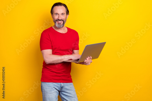 Photo of pretty charming retired man wear red t-shirt typing modern device empty space isolated yellow color background