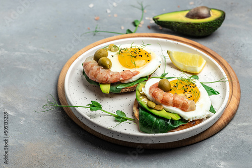 open sanwich with wholemeal bread, soft fried egg, spinach, avocado, shrimps on gray background, Ketogenic breakfast. superfood concept. Healthy, clean eating. Top view