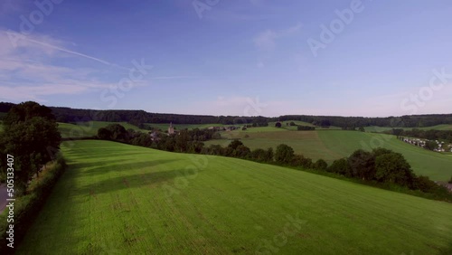 Over the rolling hills, meadows with natural fences, wooded banks, with rural roads, Beusdael Castle in the background, in South Limburg the Netherlands Aerial View photo