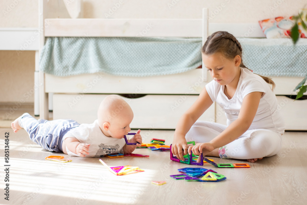Cute children infant boy and little girl playing with toy magnetic construction set at home.