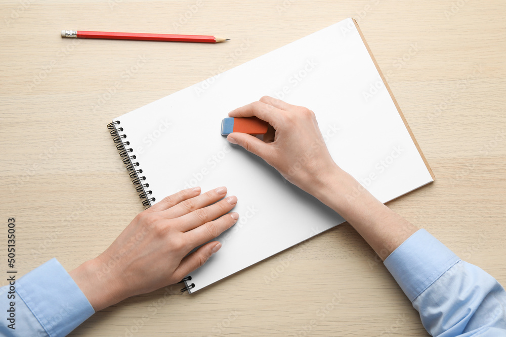 Woman erasing something in notebook at wooden table, closeup Woman erasing something in notebook at wooden table, closeup