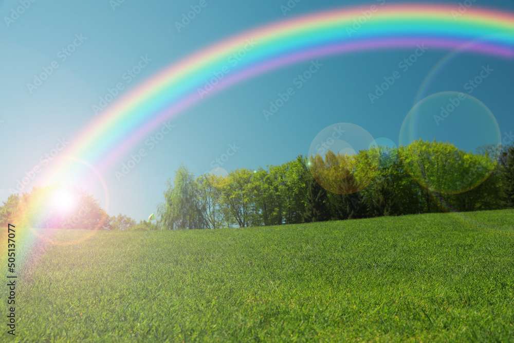 Picturesque view of green meadow and beautiful rainbow in blue sky on sunny day Picturesque view of green meadow and beautiful rainbow in blue sky on sunny day