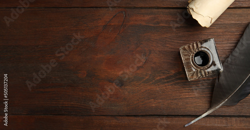 Quill, inkwell and parchment scroll on wooden table, flat lay with space for text. Banner design photo