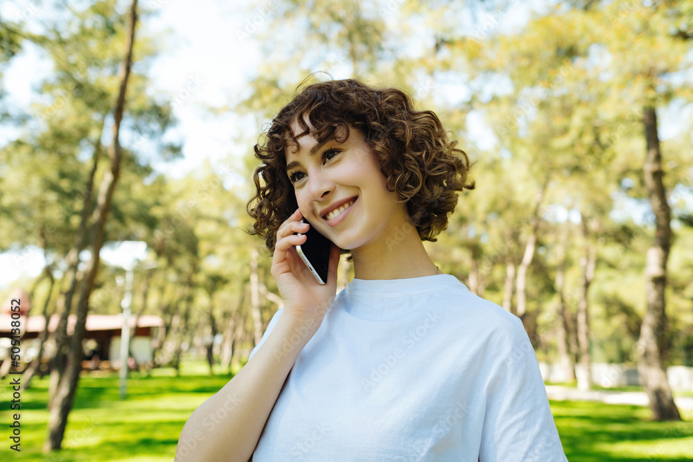Talking phone, cheerful pretty young redhead woman talking on phone and look straight ahead. Holding smartphone close to ear. Standing alone outside. Talking phone, cheerful pretty young redhead woman talking on phone and look straight ahead. Holding smartphone close to ear. Standing alone outside.