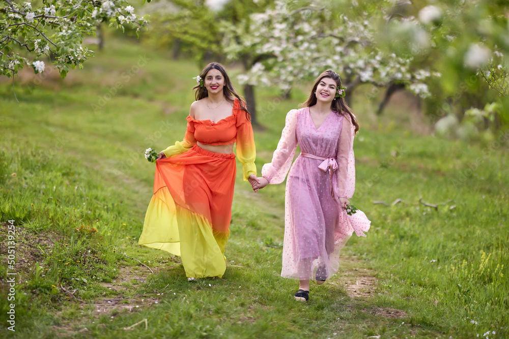 Beautiful women enjoying the garden with flowering trees, young women with flowers in the green park. cheerful teenagers walking outdoors. soft light style color