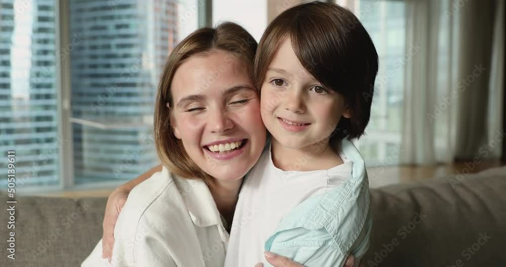 Head shot portrait beautiful mom and little 6s cute son sit together on couch at modern home, embracing smile staring at camera, look happy feeling love and attachment, close up. Mothers love concept Head shot portrait beautiful mom and little 6s cute son sit together on couch at modern home, embracing smile staring at camera, look happy feeling love and attachment, close up. Mothers love concept