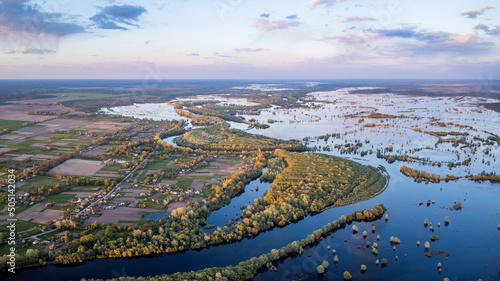 Picturesque aerial landscape of village near flooded valley of river Desna at sunset. Countryside in Ukraine, last sun rays illuminating small village on bank of river during powerful flood