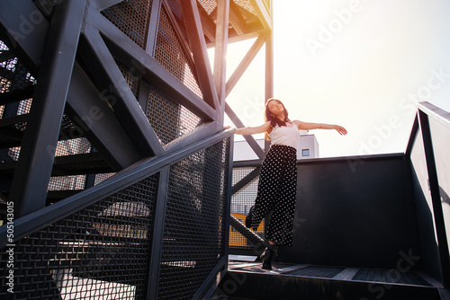 Carefree woman going downstairs on a heavy metal fire exit stairs. Holding onto a beam, swinging her body in acircle. Lit with evening sun. photo