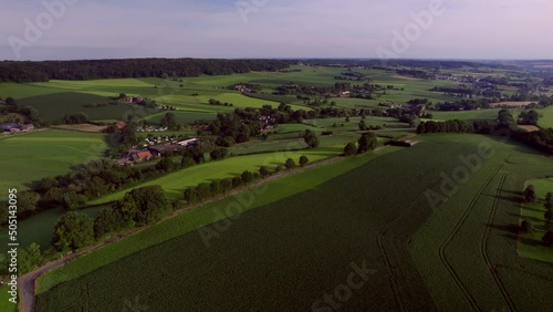 Dutch valley landscape with rolling hills and farmlands, with natural fences, wooded banks, farms, rural roads and forest in the background, in South Limburg, the Netherlands. Drone Aerial View