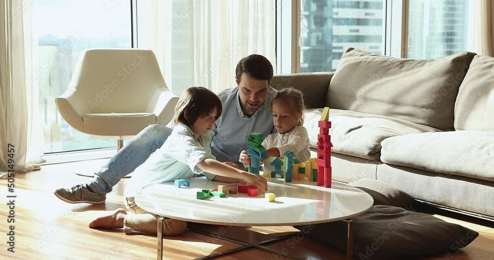 Loving young father play wooden bricks with beautiful preschoolers son and daughter in modern fashionable living room. Family weekend leisure playtime activity, children development and hobby concept Loving young father play wooden bricks with beautiful preschoolers son and daughter in modern fashionable living room. Family weekend leisure playtime activity, children development and hobby concept
