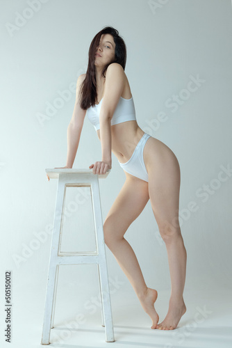 Dreamy looking girl leaning on chair, posing in white underwear isolated over grey studio background. Tendernes photo