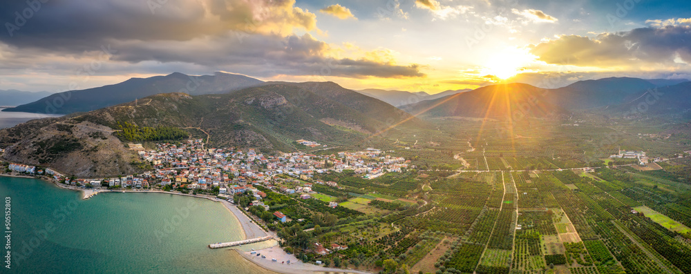 Aerial view of a small Greek village on the coast of the Mediterranean sea. Green hills of Peloponnese peninsula, Greece, Europe. Travel to Greece landscape