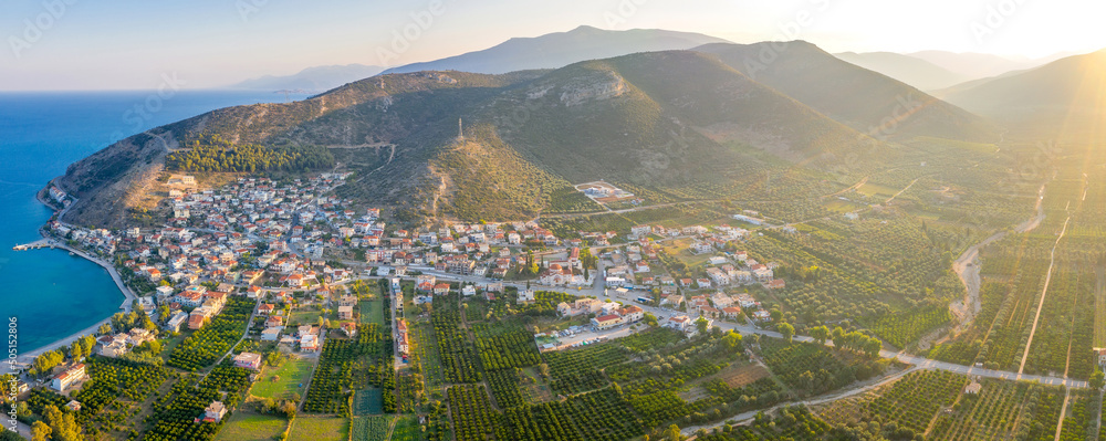 Aerial view of a small Greek village on the coast of the Mediterranean sea. Green hills of Peloponnese peninsula, Greece, Europe. Travel to Greece landscape