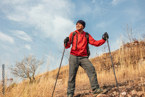 Young asian man mountaineering wearing jacket walking at outdoor. Tourist on top of the mountain walking by trekking pole. Travel adventure hiking concept.