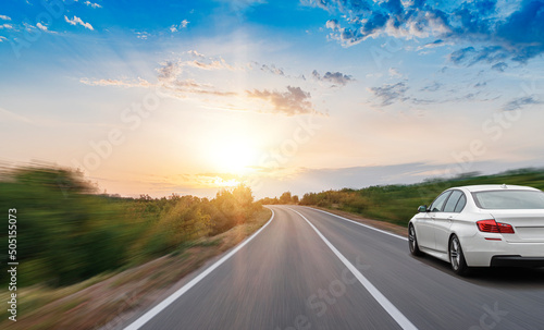 A white car drives along a beautiful road on a sunny summer day.