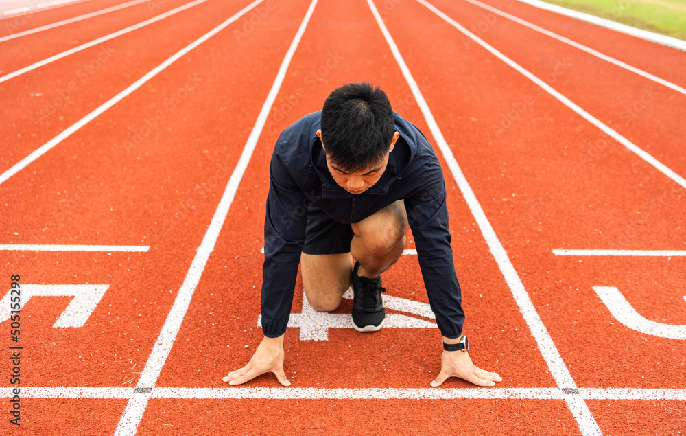 Young handsome chinese man doing star pose before running exercise on track in sport stadium. Challenge race of athletes running in the starting point