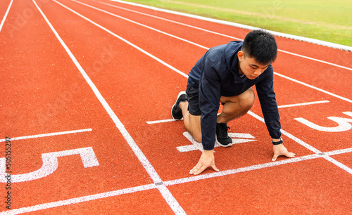 Young handsome chinese man doing star pose before running exercise on track in sport stadium. Challenge race of athletes running in the starting point © Chanakon