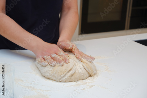 Home cooking. A young woman works with yeast dough in a modern kitchen. A young woman is kneading a dough, engaged in cooking homemade bakery. © Trik
