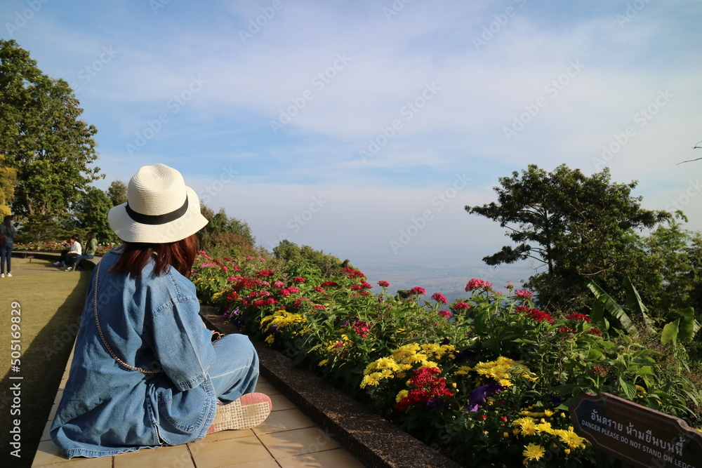 Female traveler in hat sitting in garden and looking at blue