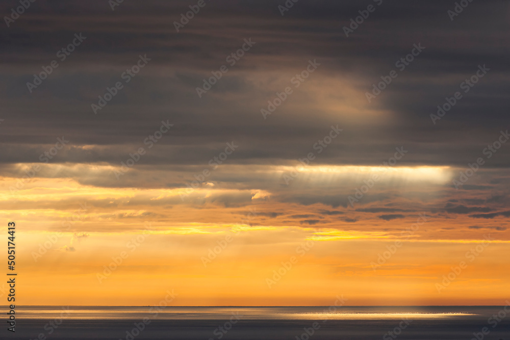 Summer sunrise with golden light breaking through nimbostratus clouds over the Irish Sea. Dublin, Ireland
