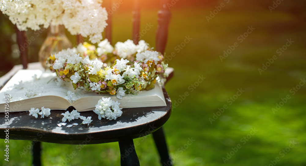 Obraz na płótnie książka, wianek i bukiet białego bzu jako kompozycja na starym krześle w słonecznym ogrodzie w salonie