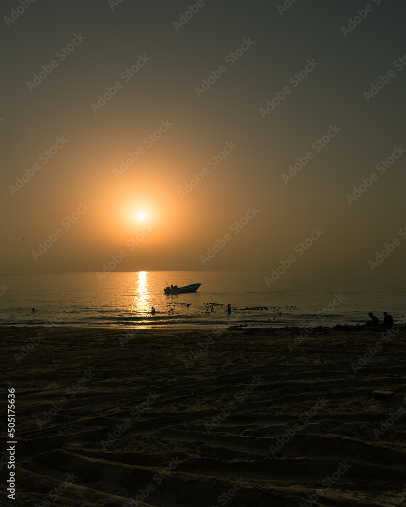 Early morning silhouetted beach with sun and fishing boat