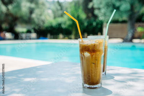 Summer holiday vacation with frappe refreshment by luxury poolside. Two ice coffee cups with straws behind resort summer pool bar. Greek fredo cappuccino cold drink at beach hotel. photo