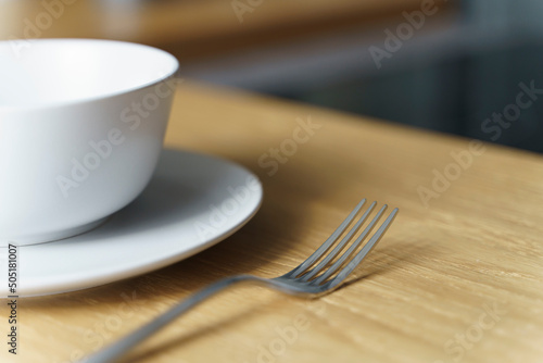 Ceramic white bowl with food and a fork on a wooden table in the kitchen in a restaurant or at home. Selected focus