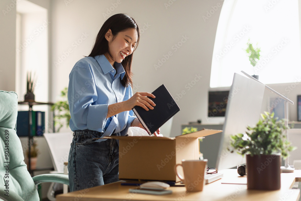 Smiling Asian woman unpacking box at new workplace Smiling Asian woman unpacking box at new workplace