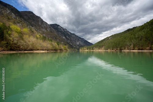 Cruise on the river Drina. The beautiful green waters reflect the mountain hills and the cloudy sky. © Petia
